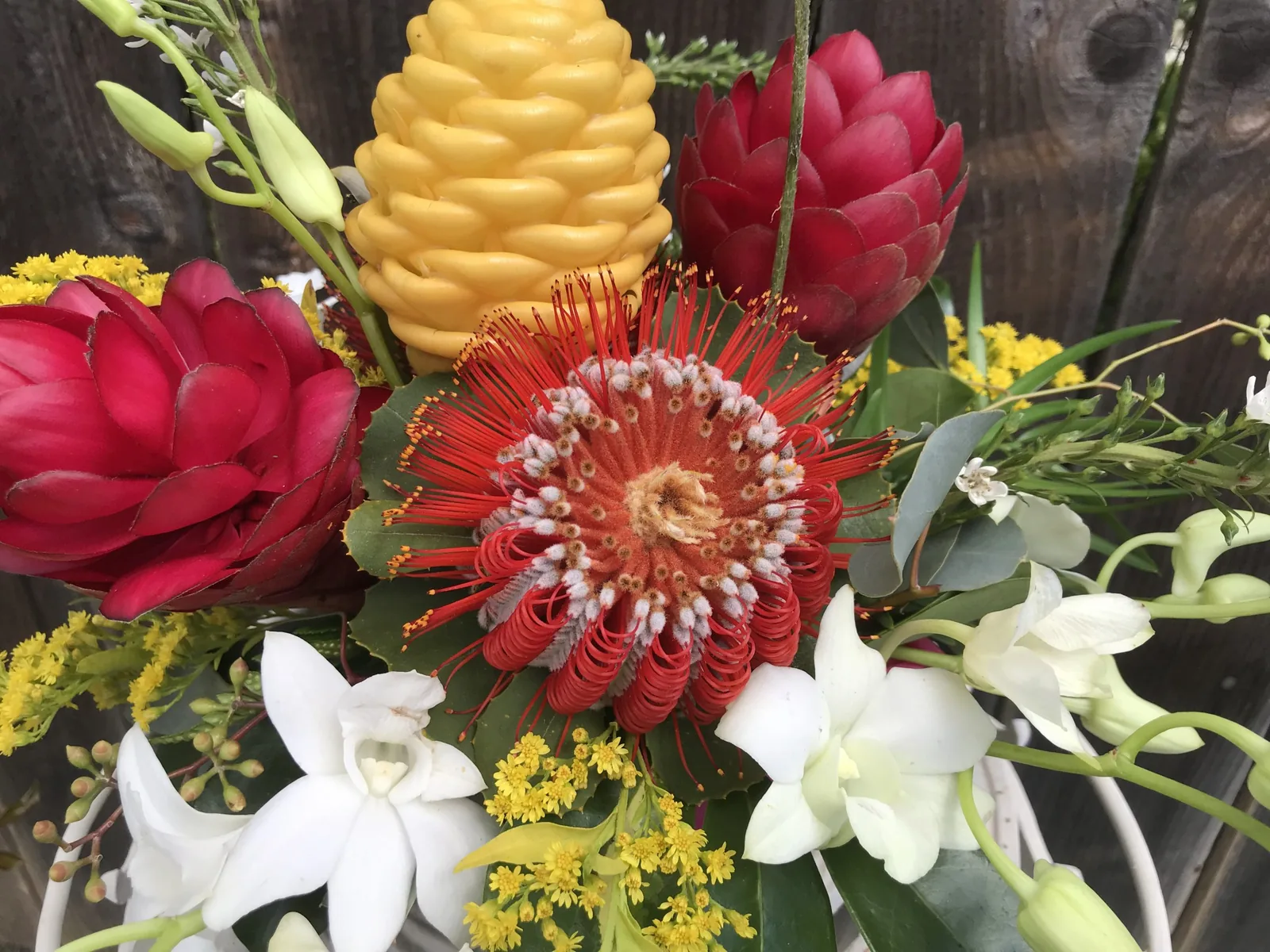 Close mixed arrangement of red ginger, golden shampoo ginger, red pincushion protea and white orchids